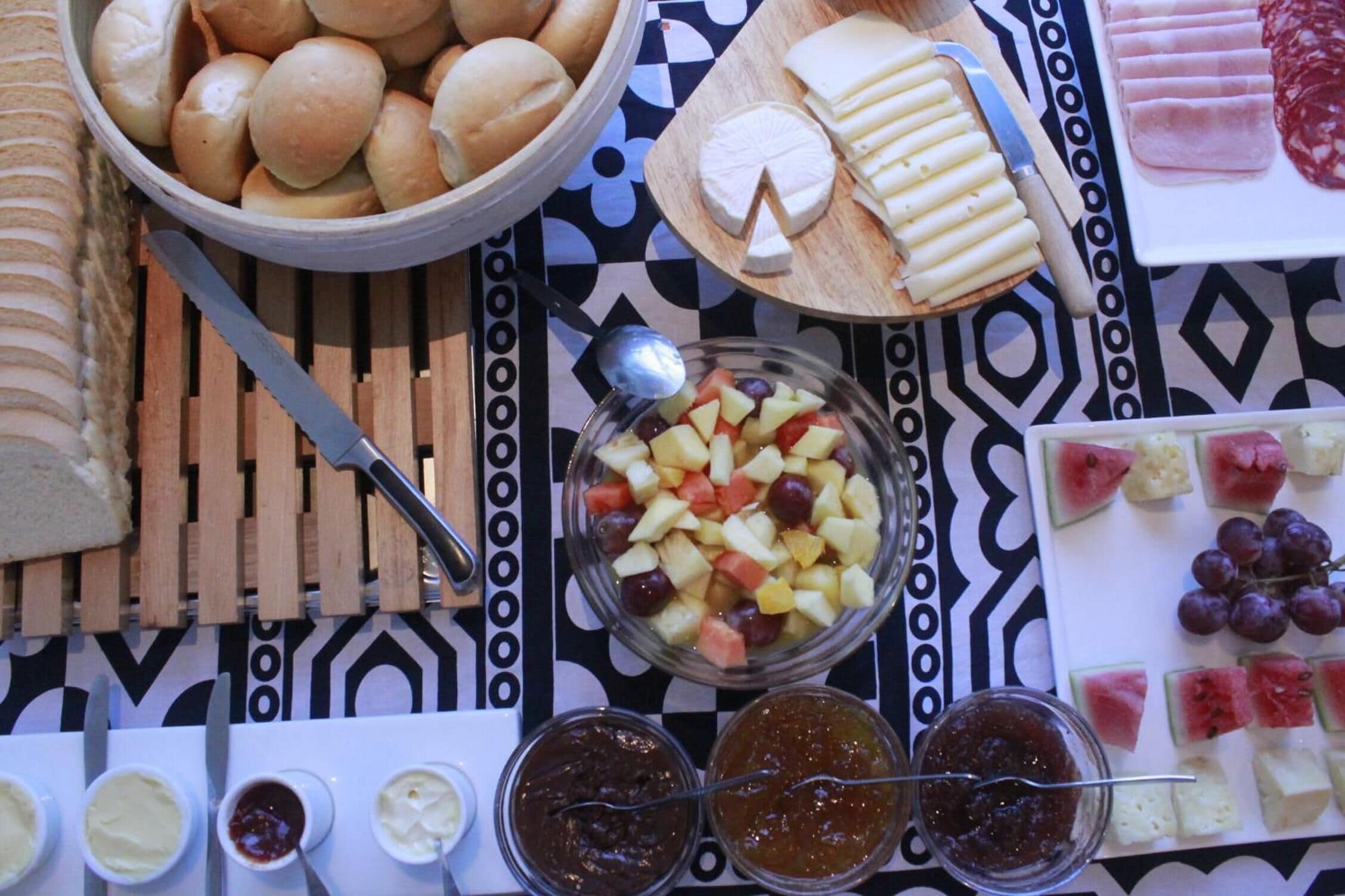 Una mesa con diferentes alimentos, como pan, queso, frutas y mermeladas.