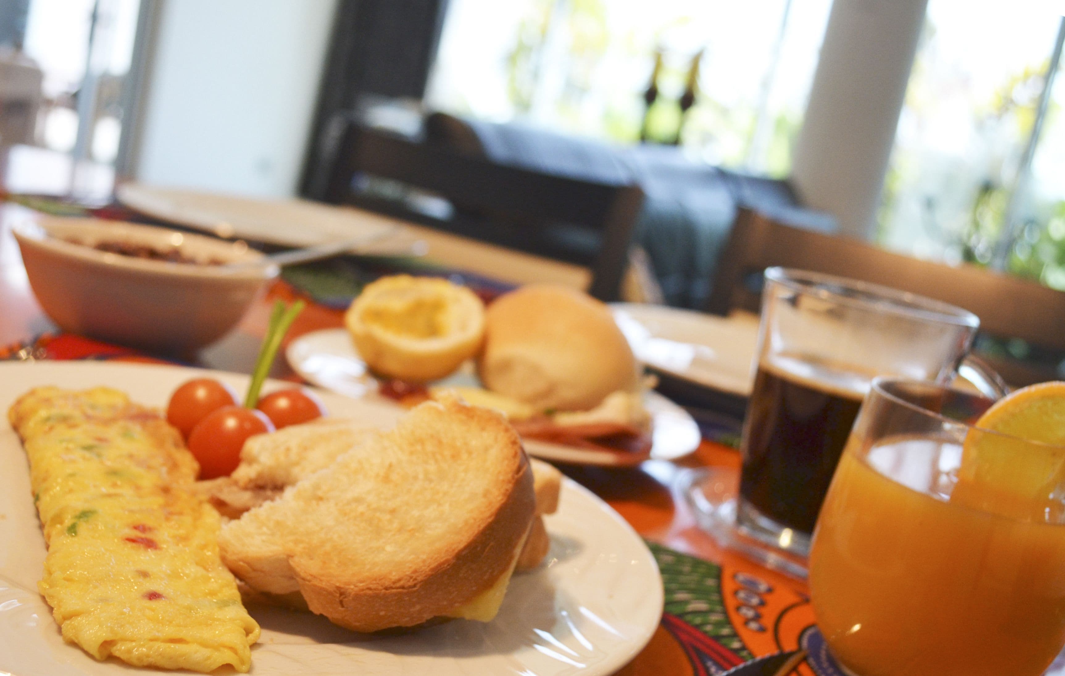 Une table mise pour le petit-déjeuner avec une omelette, des toasts, des tomates, un sandwich et un verre de jus d’orange.