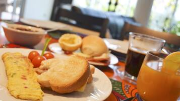 A breakfast setting with an omelet, toast, tomatoes, a sandwich, and a glass of orange juice on a table.