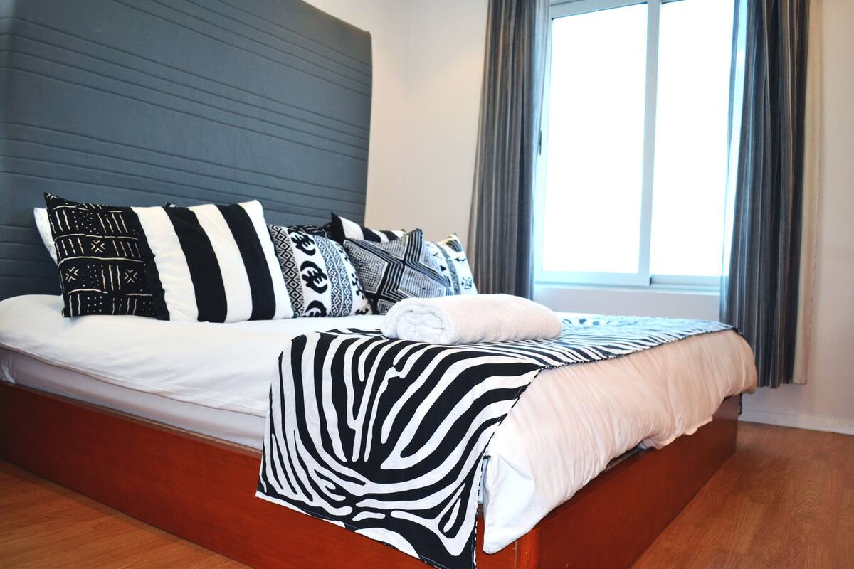 A bed with a zebra-patterned blanket, a headboard, and multiple pillows with various patterns.