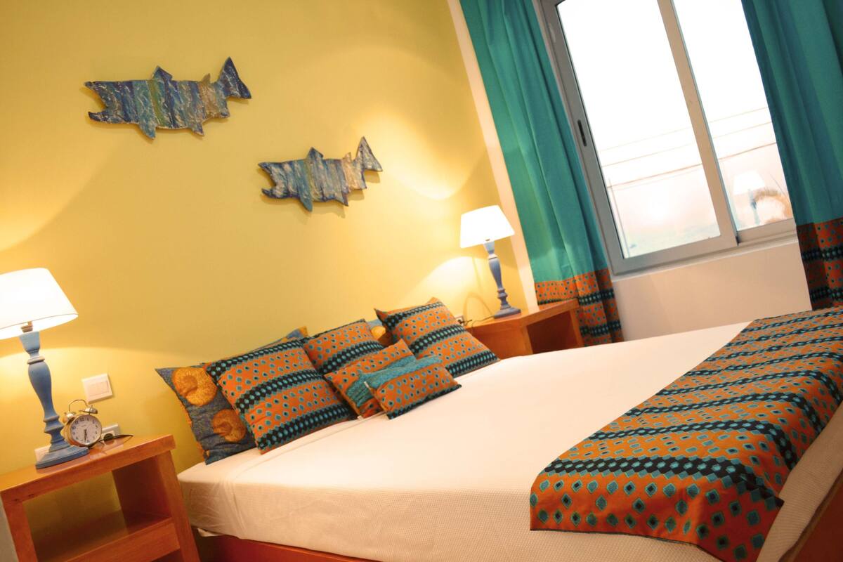 A hotel room with a bed, two nightstands, a lamp, a clock, and a window with curtains.