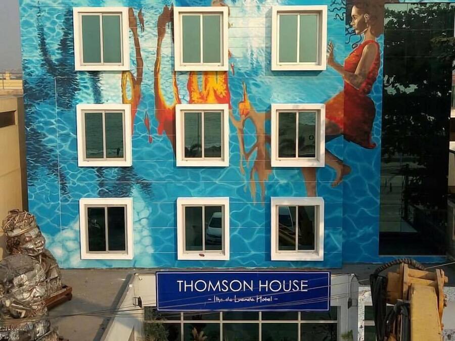A building facade with a mural of a woman in a red dress, windows, and a sign reading "Thomson House."