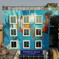 Fachada de edifício com um mural de uma mulher num vestido vermelho, janelas e um letreiro com a inscrição 'Thomson House'.