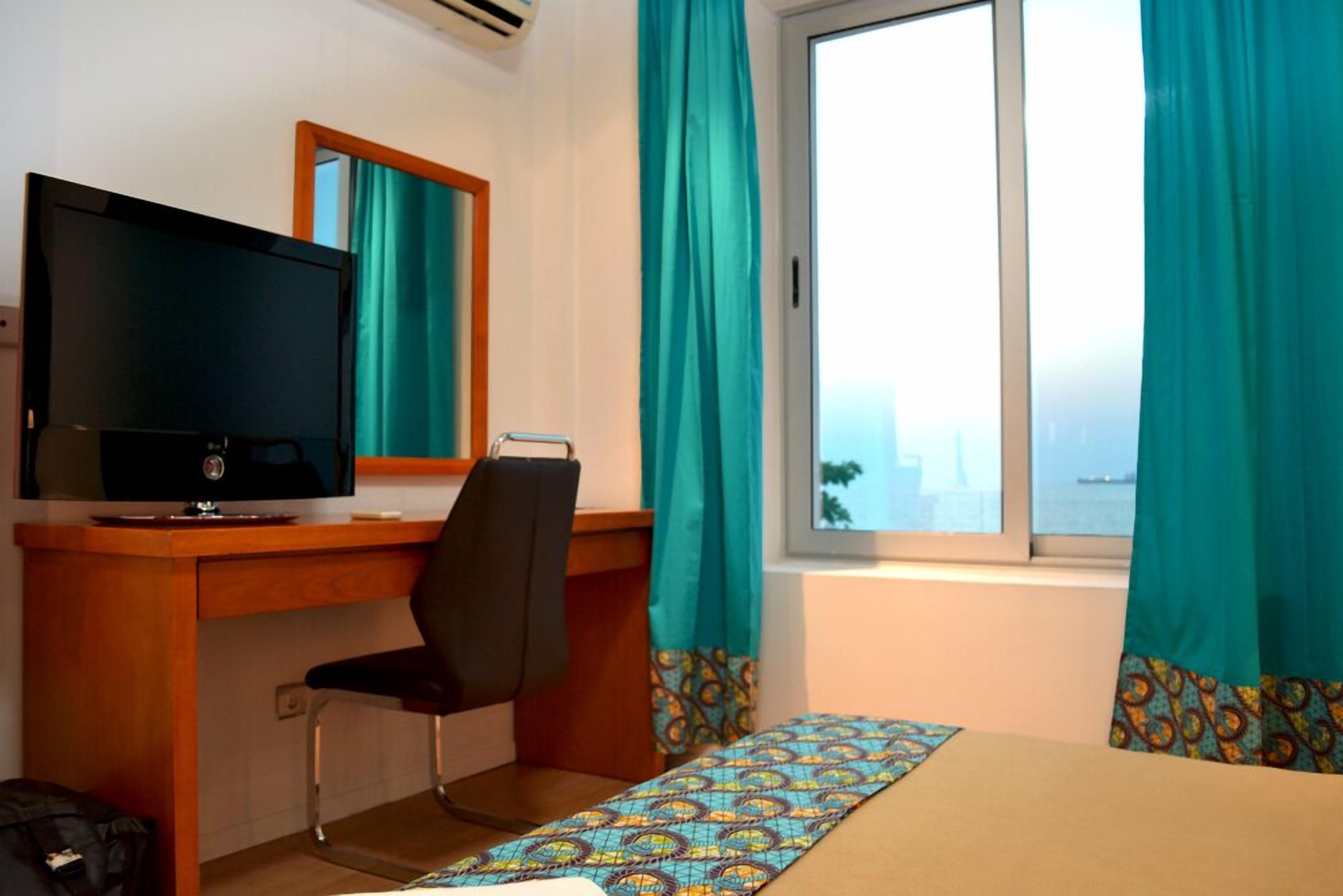 Une chambre d’hôtel avec un lit, un bureau avec une télévision, une chaise et une fenêtre avec des rideaux.