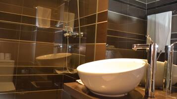 A modern bathroom with a large white basin, chrome fixtures, and dark tiled walls.