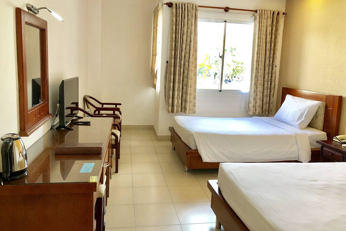 A hotel room with a bed, a desk with a chair, a television, and a window with curtains.