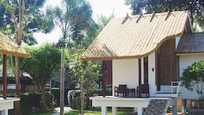 A bungalow with a thatched roof, a covered outdoor seating area, and a well-maintained garden. - Pai Country Hut (Pai)