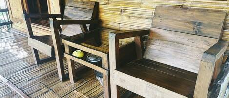 A wooden bench with a woven wall backdrop, a woven floor, and a small shelf with a yellow pot and a bowl.