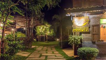 A well-lit outdoor area with a pathway leading to a building labeled "Prai Country Hut."