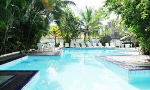 Un área de piscina con varias piscinas, rodeada de palmeras y tumbonas.