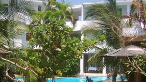 A pool area with palm trees and umbrellas, surrounded by a building with multiple balconies. - The white Haven (Panadura)