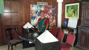 A reception area with a wooden reception desk, a colorful abstract painting, and a framed bird painting on the wall. - The white Haven (Panadura)