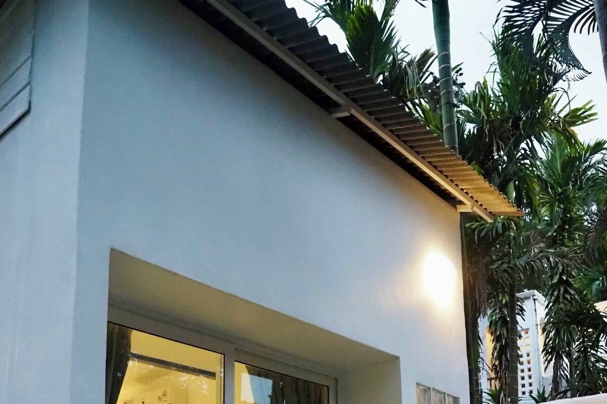 Un edificio con puerta corrediza de vidrio que da a una habitación con cama y una mesita. Hay dos gatos en el porche.