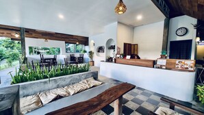 A modern reception area with a wooden reception desk, a clock, and a seating area with a bench and chairs. - Canary Guesthouse (Pai)