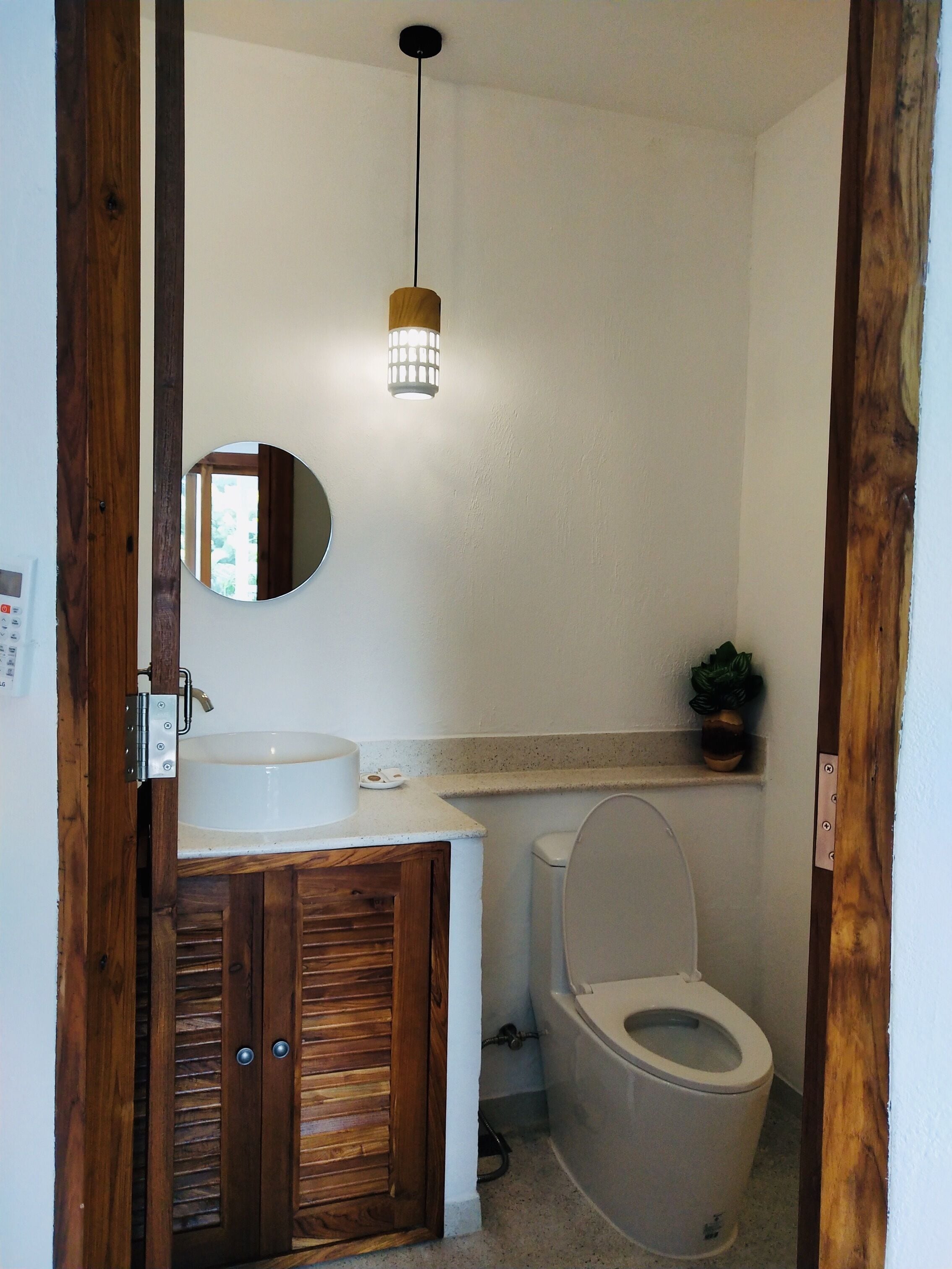 A bathroom with a wooden cabinet, a sink, a toilet, a mirror, and a hanging light fixture.