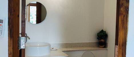 A bathroom with a wooden cabinet, a sink, a toilet, a mirror, and a hanging light fixture.