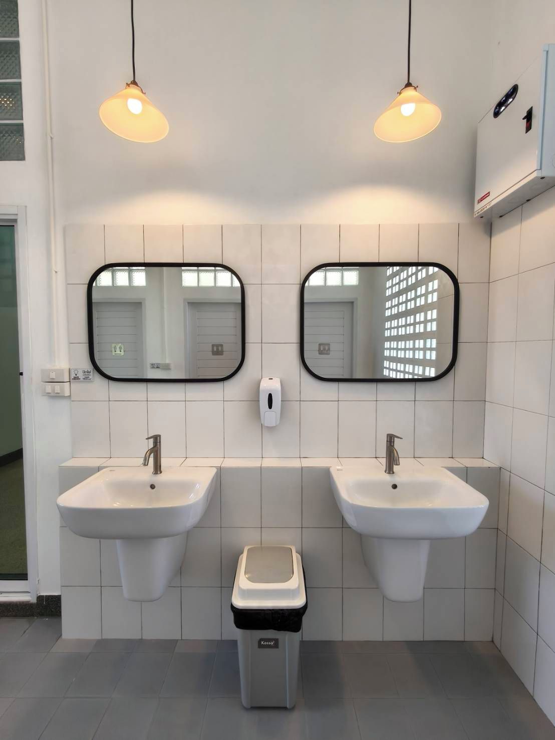 A modern bathroom with two sinks, a trash bin, and two pendant lights.
