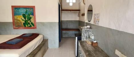 A hotel room with a bed, a small table, a mirror, and a painting on the wall.