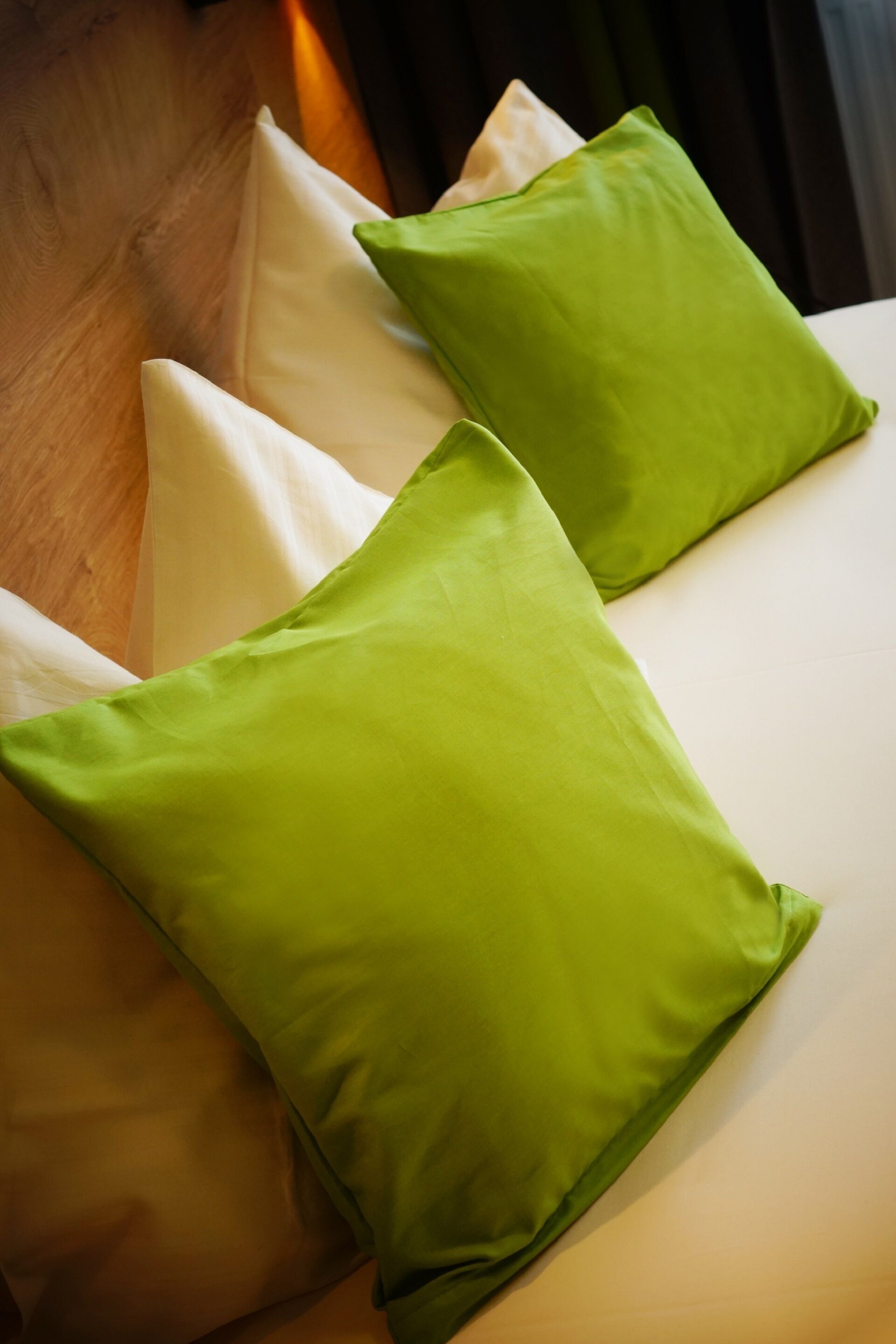 A bed with two green pillows and a white pillow.