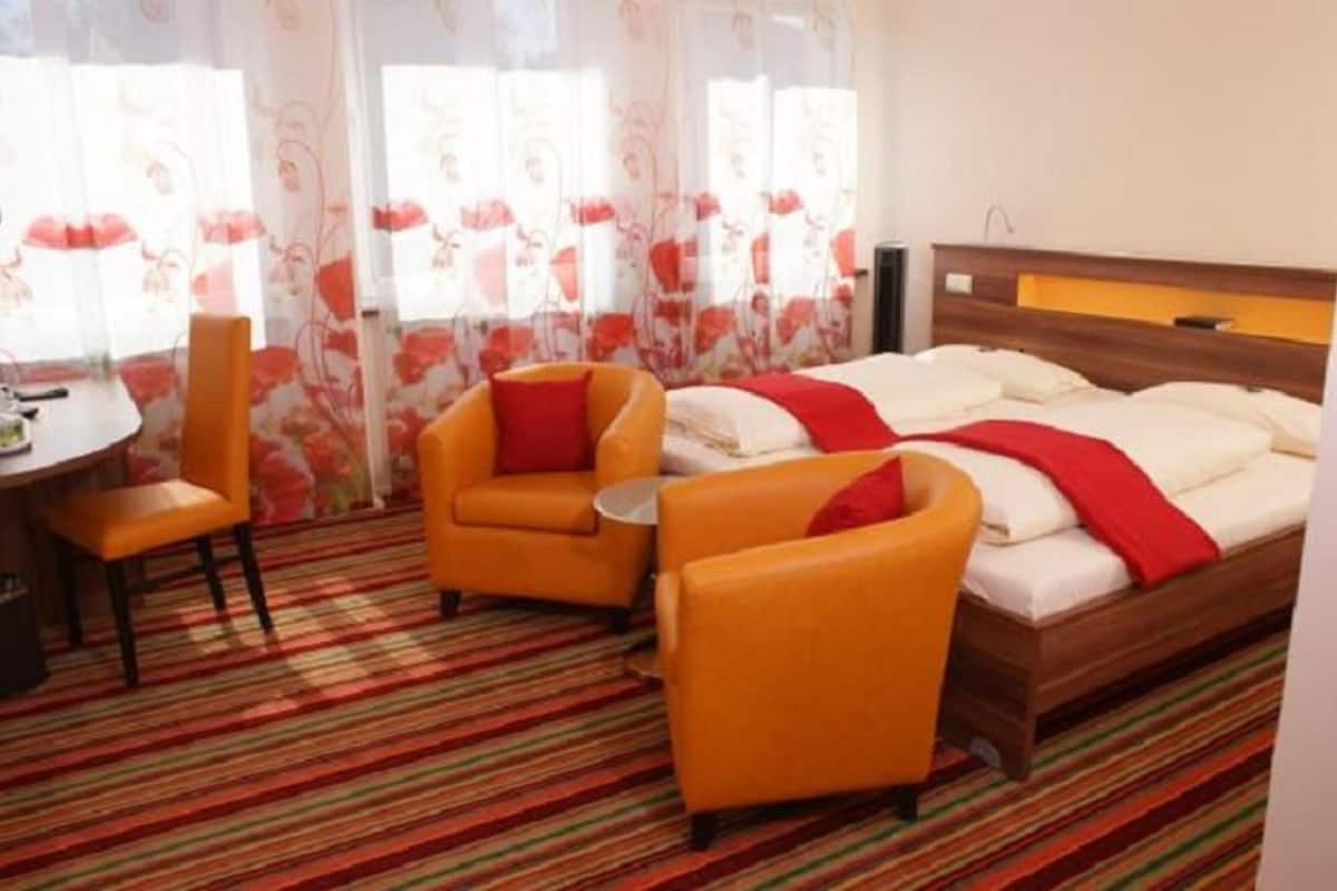 A hotel room with a bed, two armchairs, a small table, and a desk.
