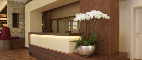 A reception area with a wooden reception desk, a potted plant, and a stone wall.