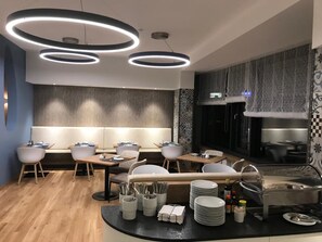 A modern restaurant with a central seating area, a buffet station, and a kitchen visible through a glass partition. - Hotel Peterhof (Kempten)