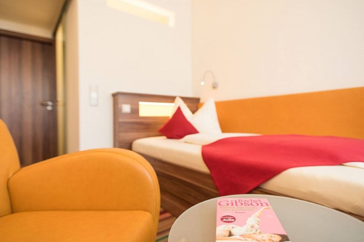 A hotel room with a bed, a red pillow, and a magazine on the bed.