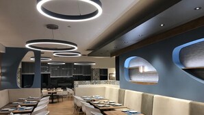 Een modern restaurantinterieur met ronde plafondlampen, houten tafels, witte stoelen en een blauwe accentmuur met een raam.