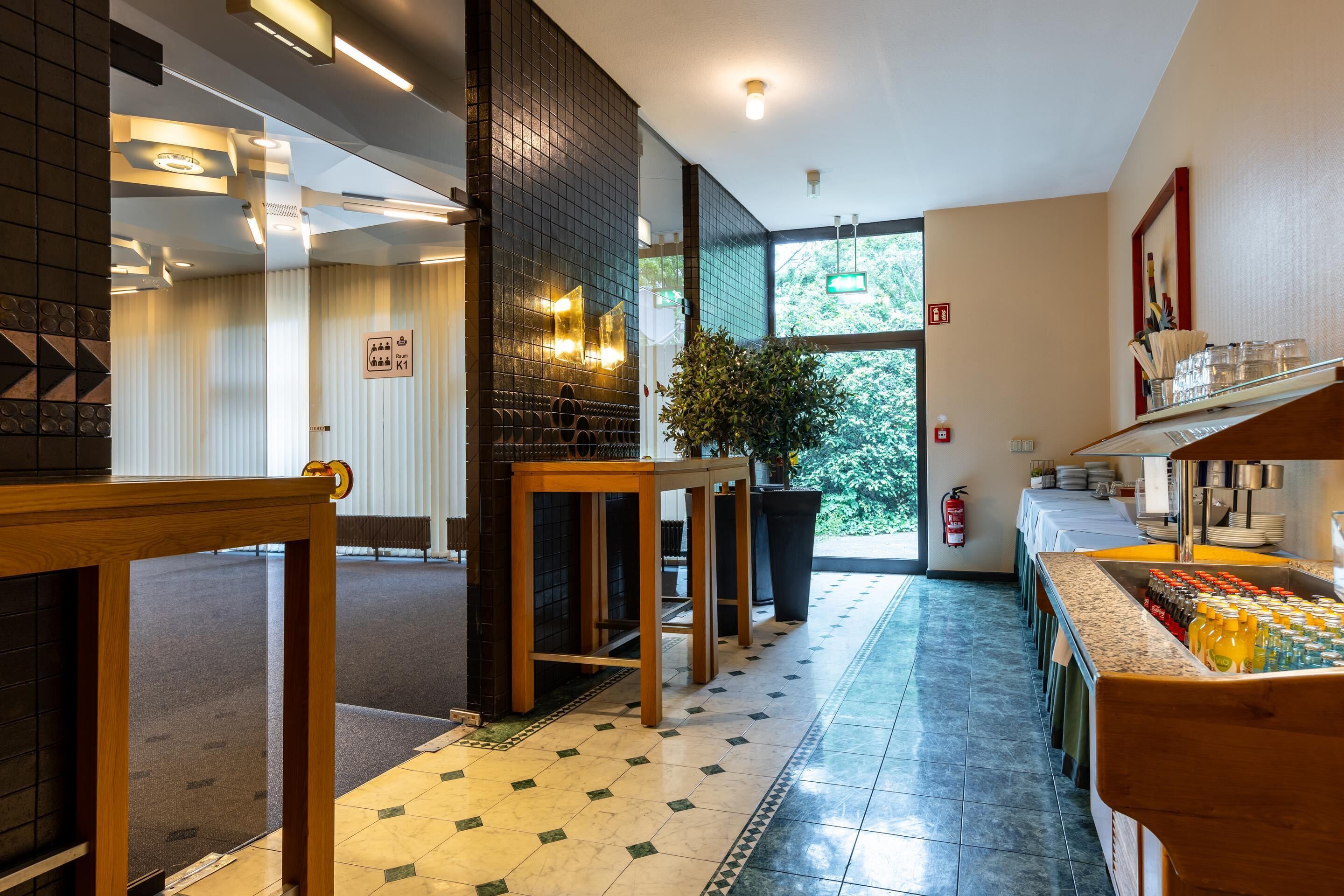 Un hall d’hôtel moderne avec un long comptoir d’accueil, un espace dédié au café et une grande fenêtre donnant sur l’extérieur.