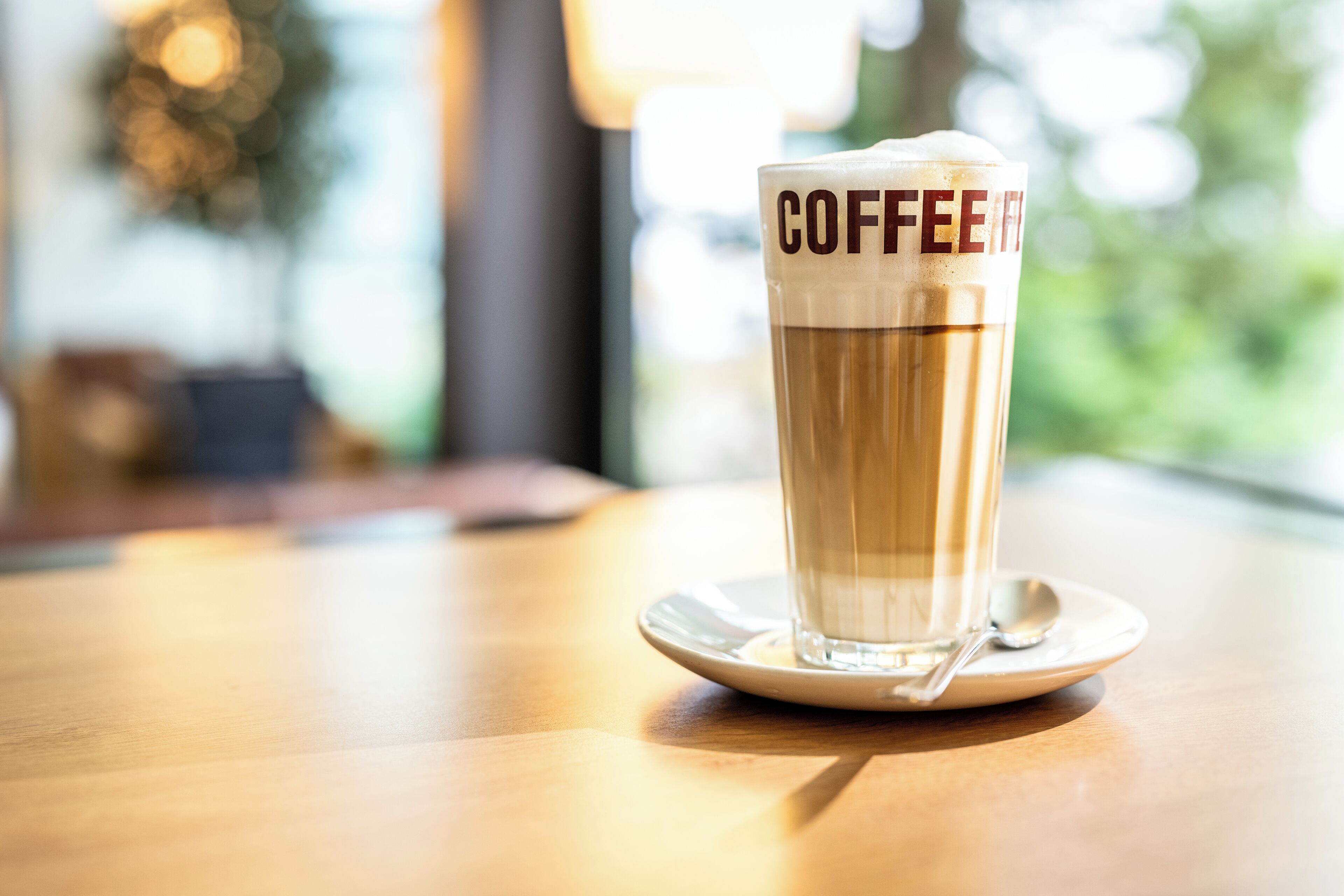 Une tasse de café posée sur une soucoupe, avec une cuillère, le tout sur une table en bois.