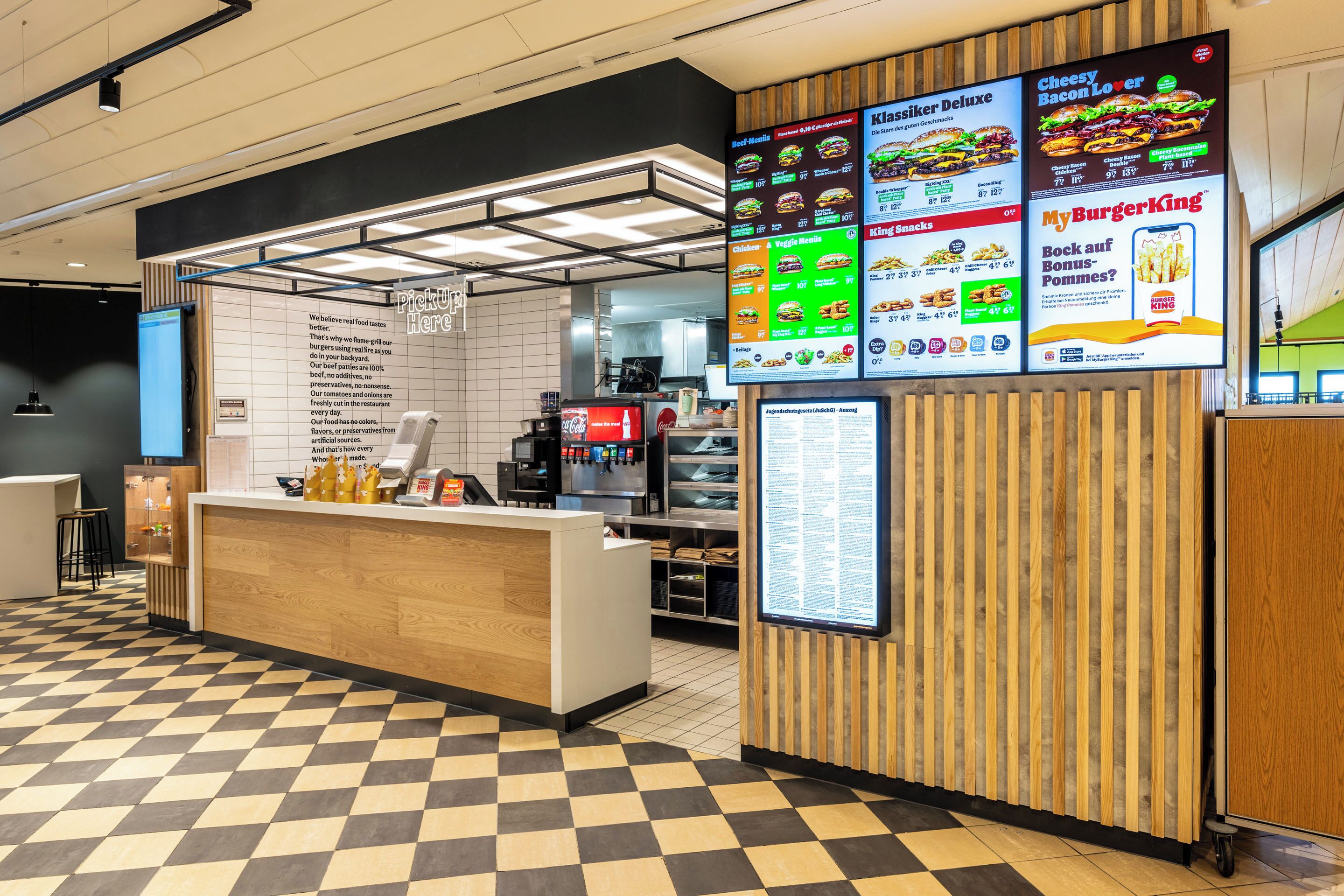 A fast-food restaurant interior with a checkered floor, a counter with a menu board, and a coffee machine.
