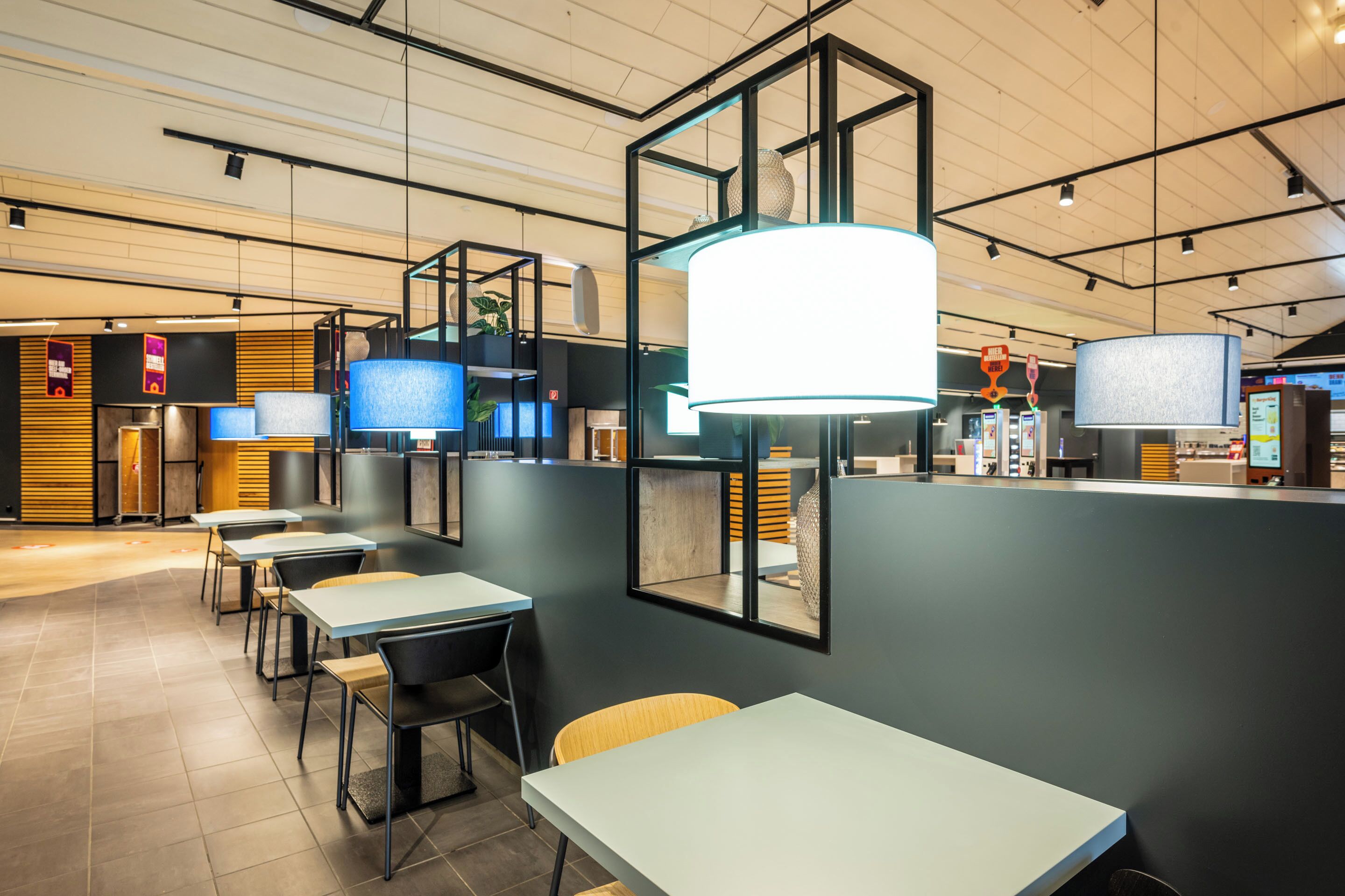 A modern restaurant interior with tables, chairs, and hanging pendant lights.