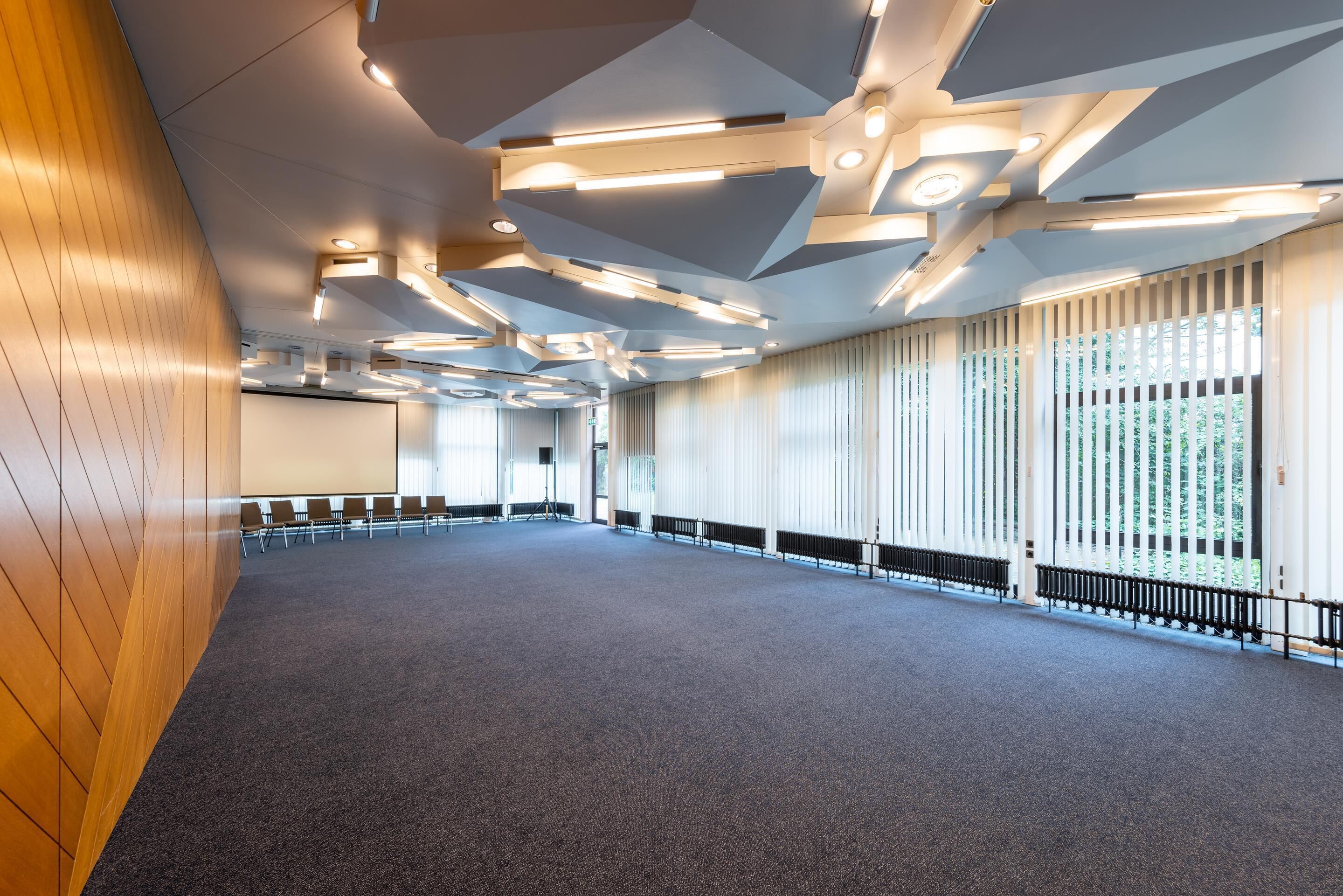 A spacious conference room with a high ceiling, modern lighting fixtures, and large windows.