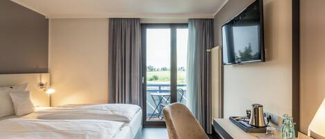 Habitación de hotel con dos camas, televisión, escritorio con cafetera y vistas al exterior.
