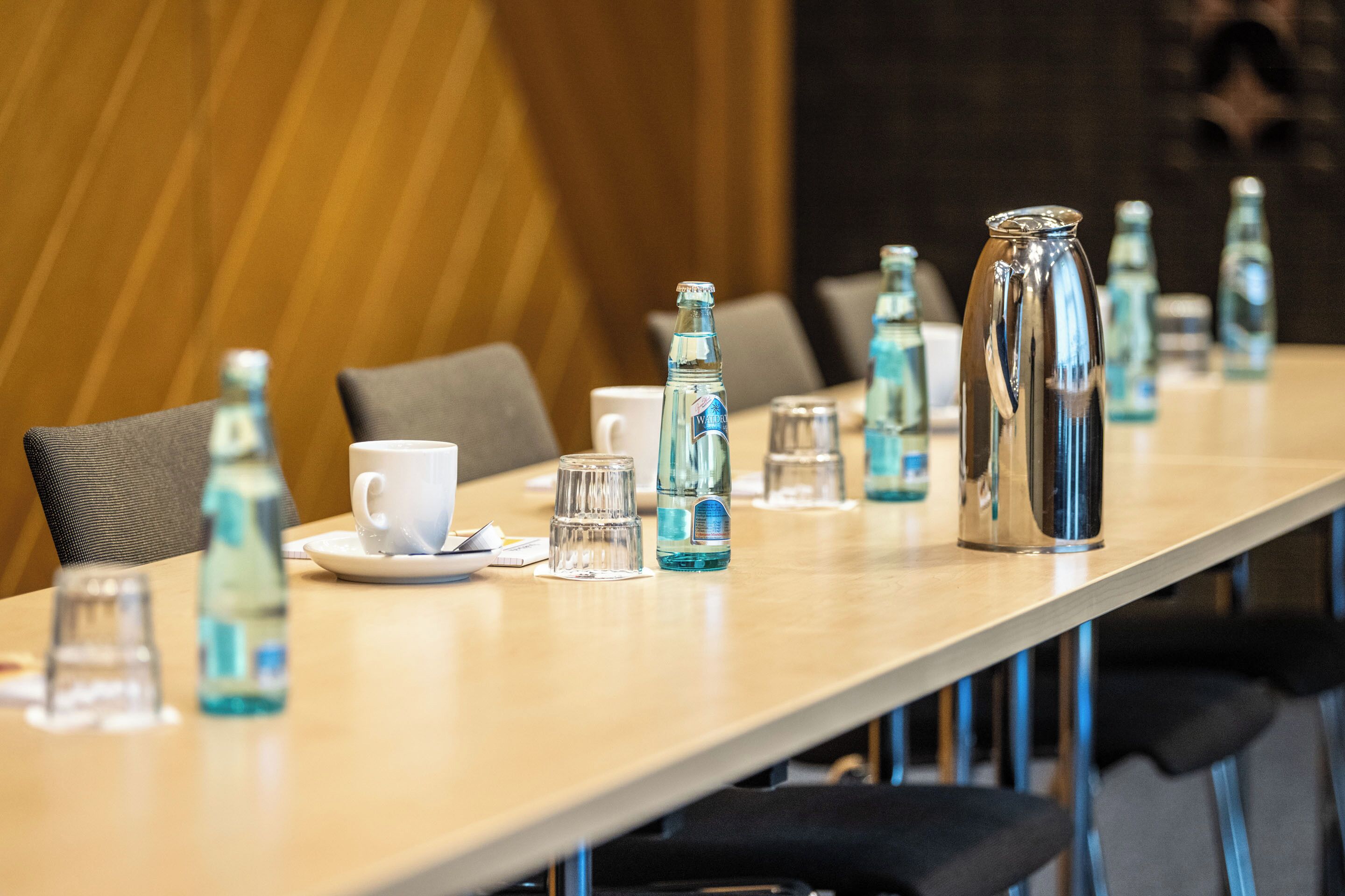 Una mesa de conferencias dispuesta con botellas de agua, vasos y una taza blanca.