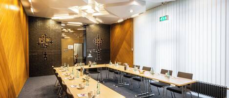 A conference room with a long table, chairs, and a tiled wall.