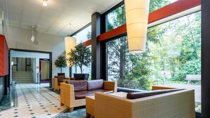 Een moderne lobby met rieten meubels, grote ramen en uitzicht op groen.