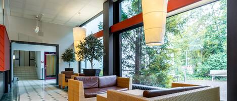 A modern lobby with wicker furniture, large windows, and a view of greenery outside.