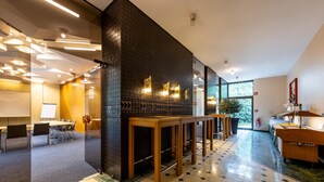 Een moderne hotelentree met een vergaderruimte, houten tafels en een grote spiegel.