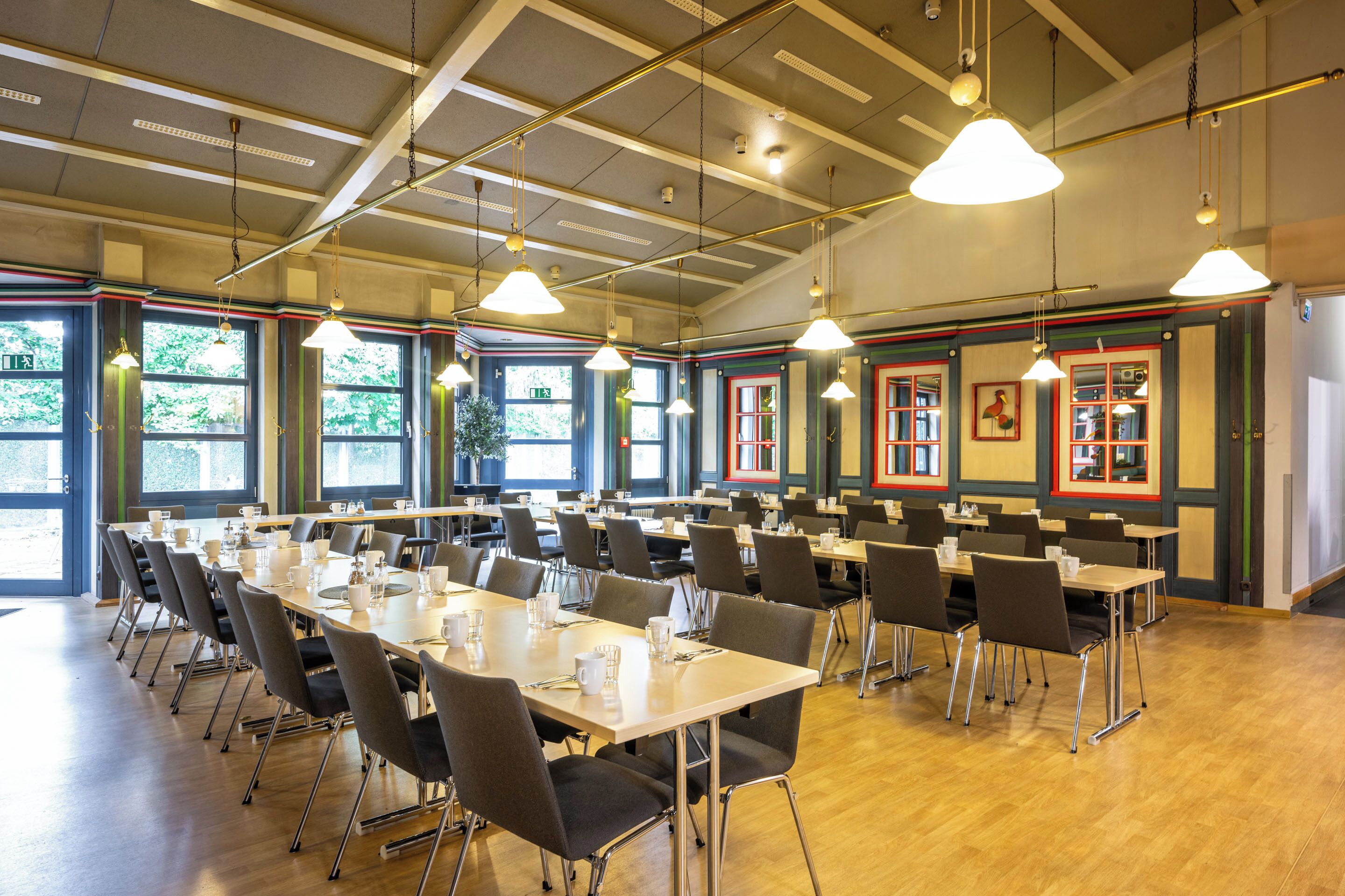 A conference room with multiple tables and chairs, large windows, and hanging pendant lights.