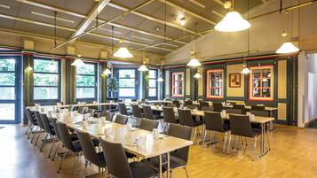 A conference room with multiple tables and chairs, large windows, and hanging pendant lights.