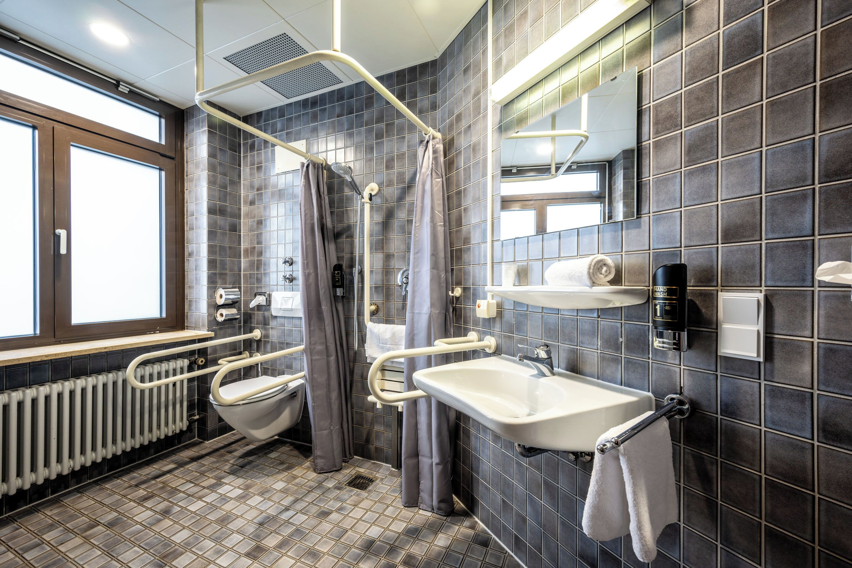 Une salle de bain moderne équipée d’une douche, de deux lavabos, de toilettes et d’une fenêtre.