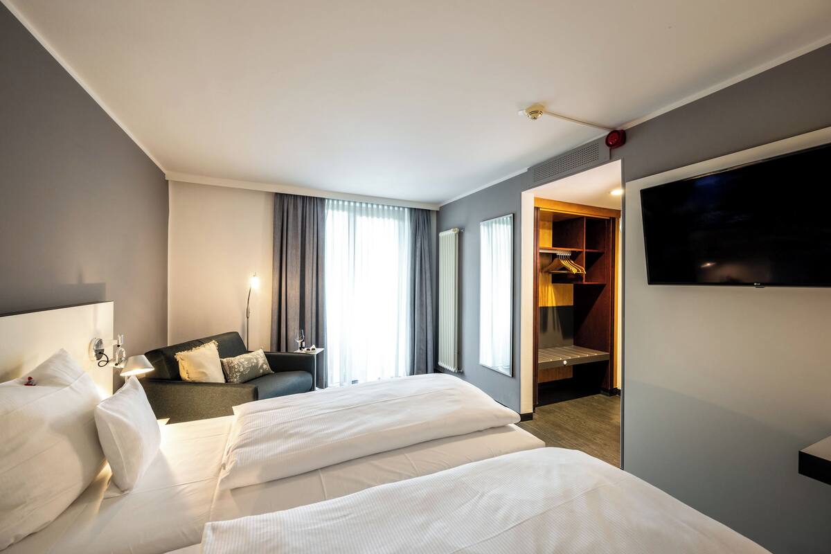Een hotelkamer met twee bedden, een bank, een televisie, een bureau met een lamp en een kledingkast.