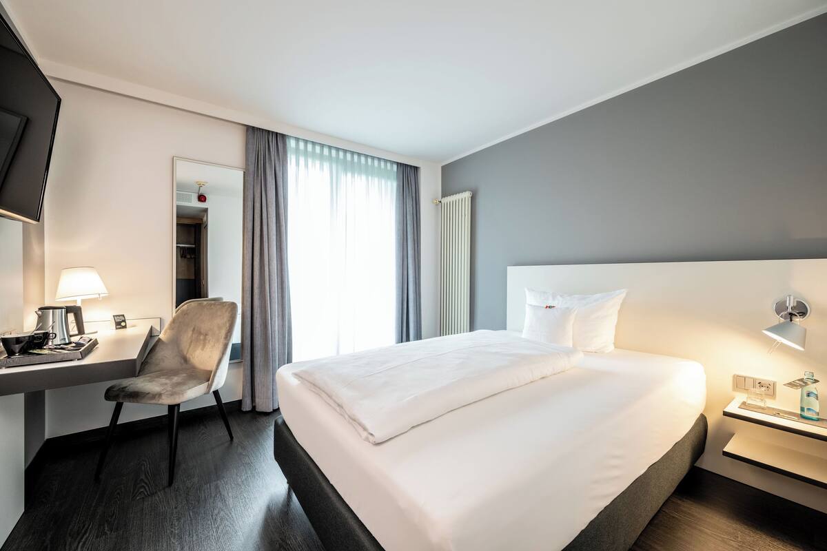 Een hotelkamer met een bed, een bureau met lamp, een stoel en een nachtkastje met lamp.