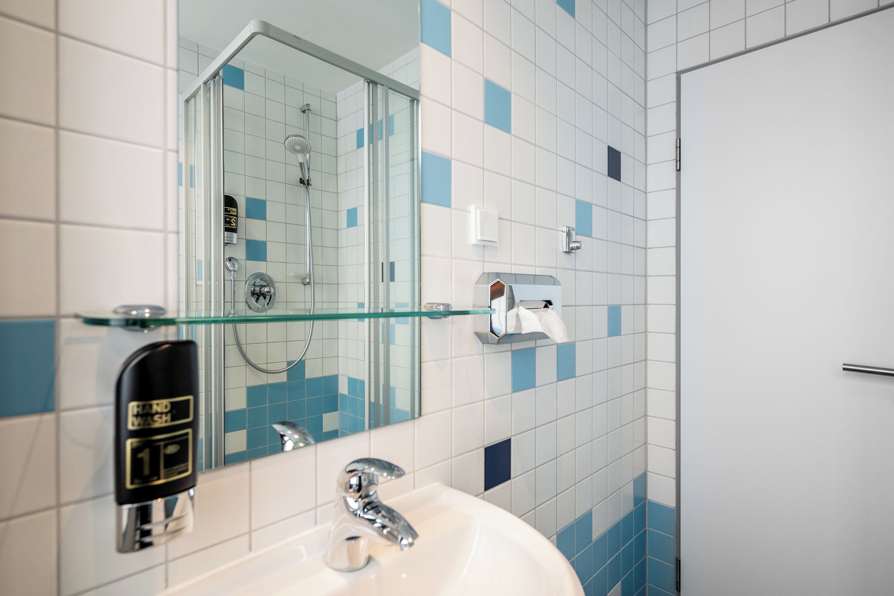 A bathroom with a glass shower enclosure, a white sink with a chrome faucet, and a mirror reflecting the shower area.
