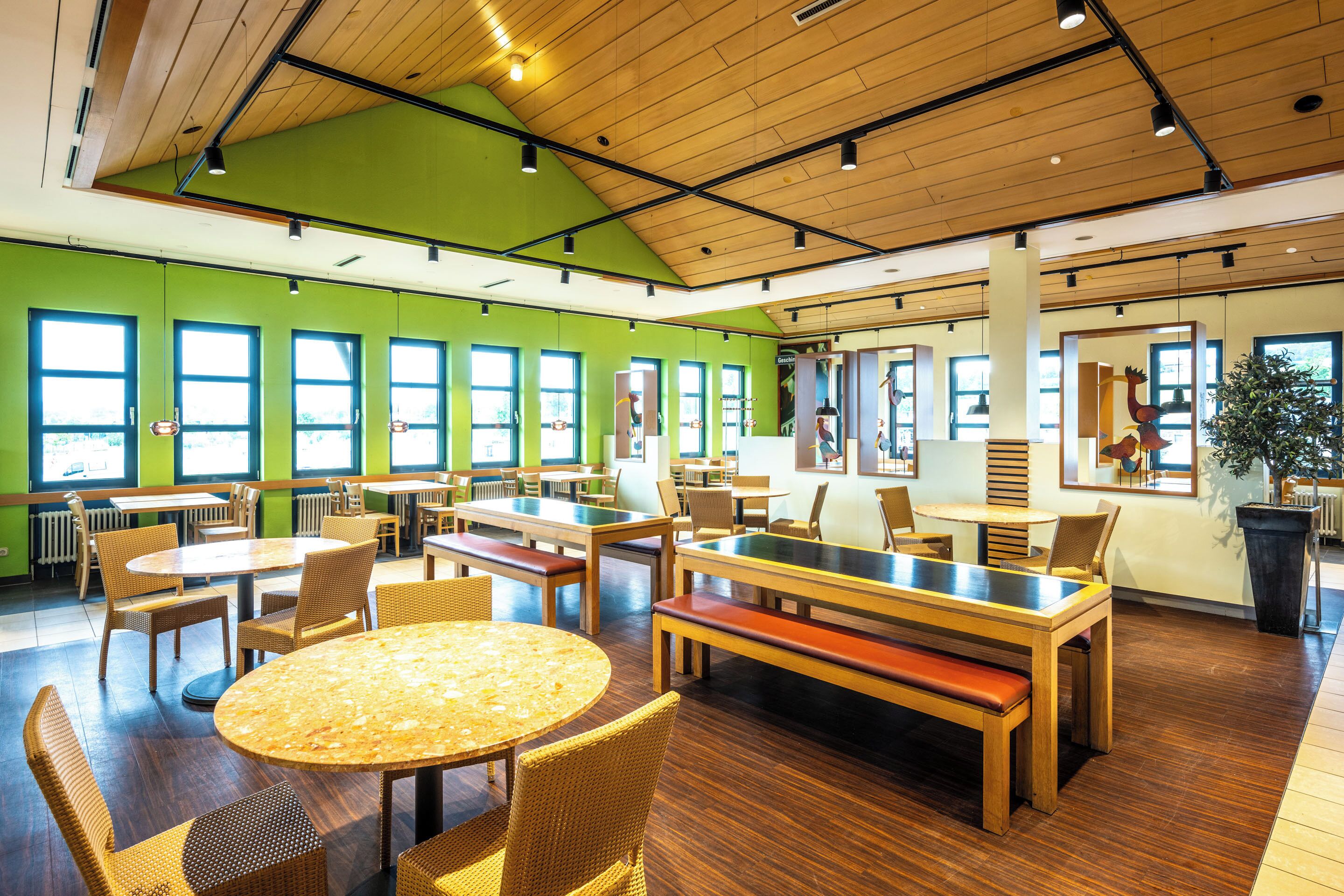 A spacious indoor dining area with multiple tables and chairs, large windows, and wooden flooring.