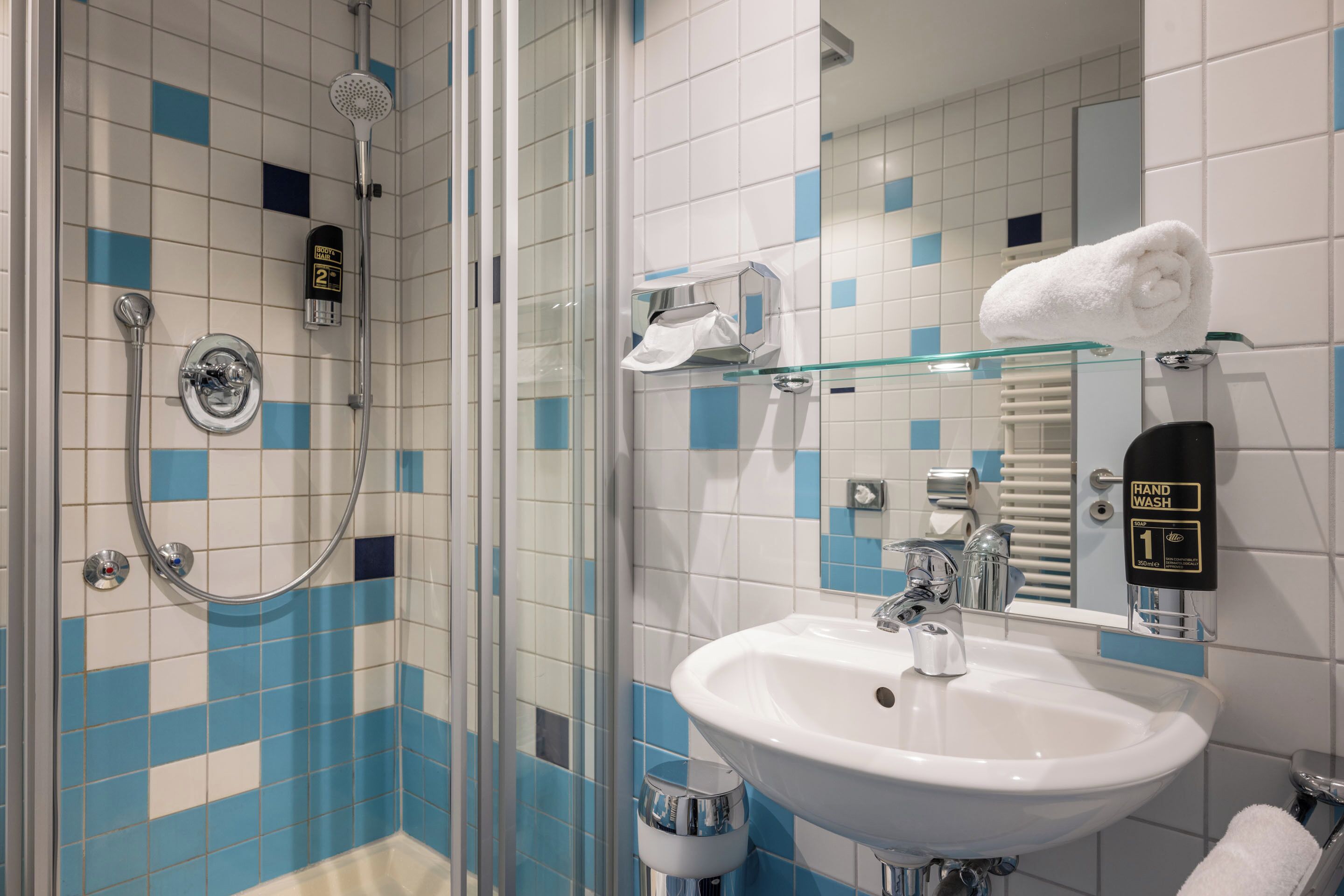 A bathroom with a glass shower enclosure, a white sink, and a hand sanitizer dispenser.