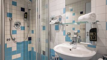 A bathroom with a glass shower enclosure, a white sink, and a hand sanitizer dispenser.