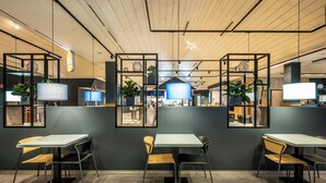 Een modern café met tafels en stoelen, een houten plafond en decoratieve planten.