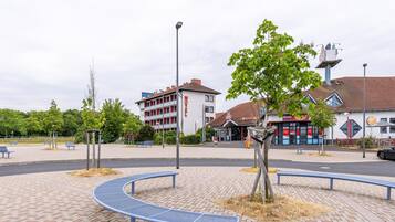 A motel with a red and white facade, a parking area, and a small park with benches and a tree.